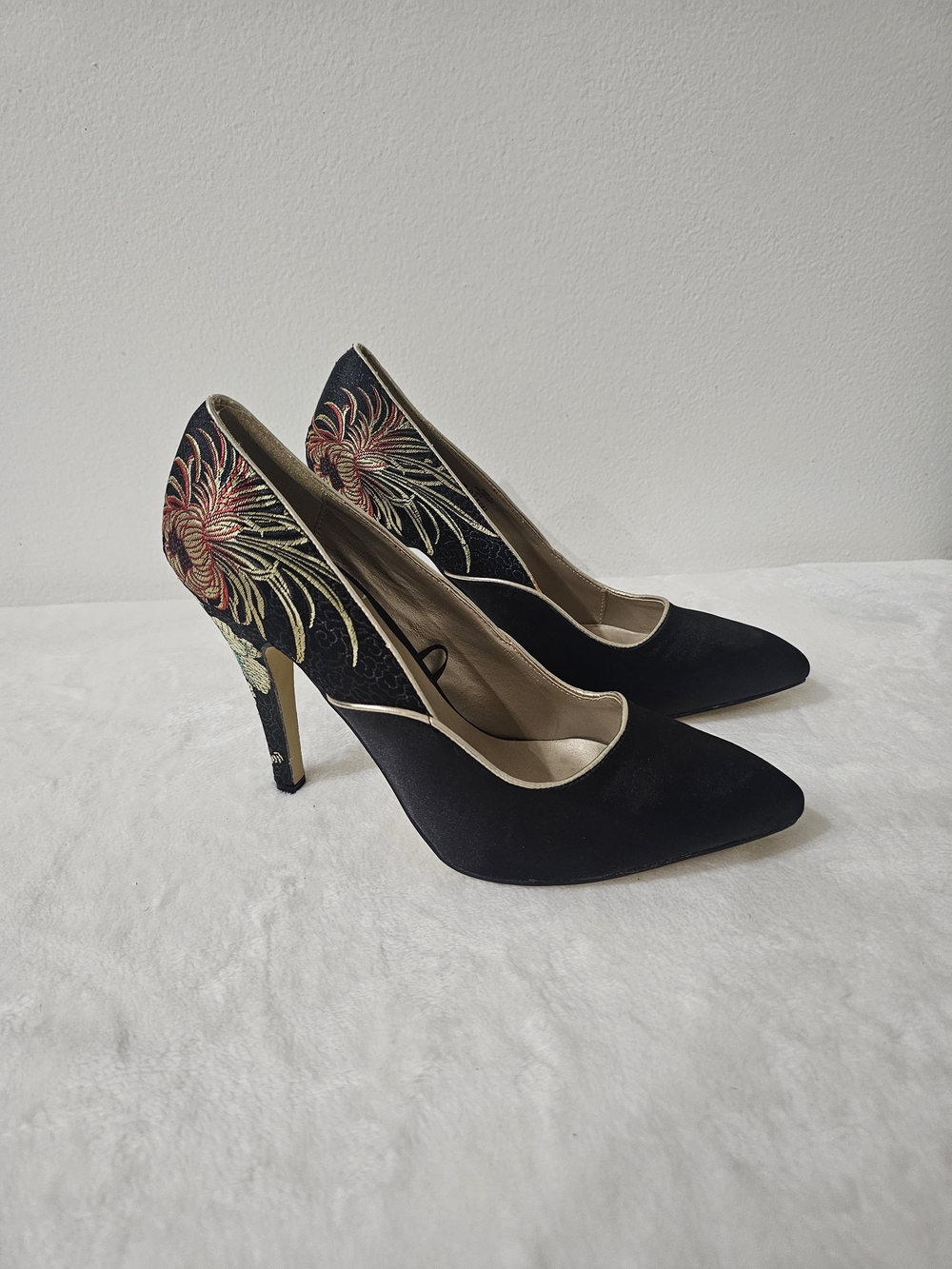 Black high-heeled shoes with a pointed toe and detailed floral embroidery on the